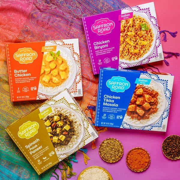 Butter Chicken Frozen Meal package, Chicken Biryani package, Chicken Tikka Masala package, Spinach Palak Paneer package on a bright Indian textile with spices 