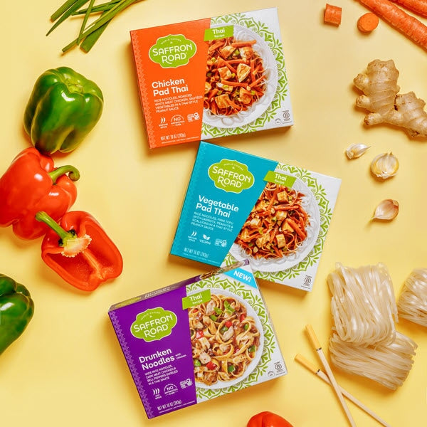 Chicken Pad Thai frozen meal package, Vegetable Pad Thai Frozen Meal package, Drunken Noodles frozen meal package on a yellow background with ingredients (noodles, vegetables) surrounding